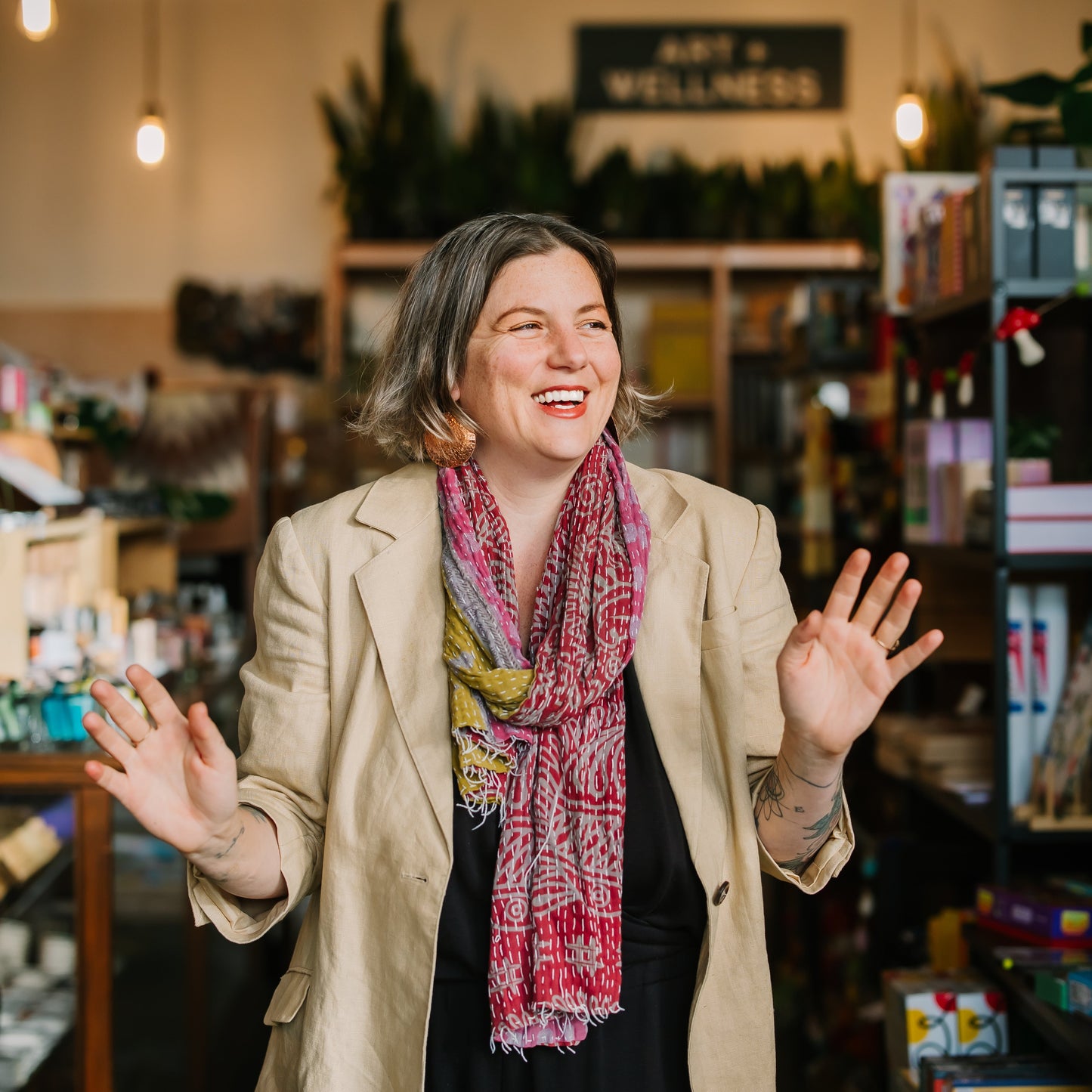 Woman in a store wearing a beige coat and colorful scarf, with a warm and inviting atmosphere.